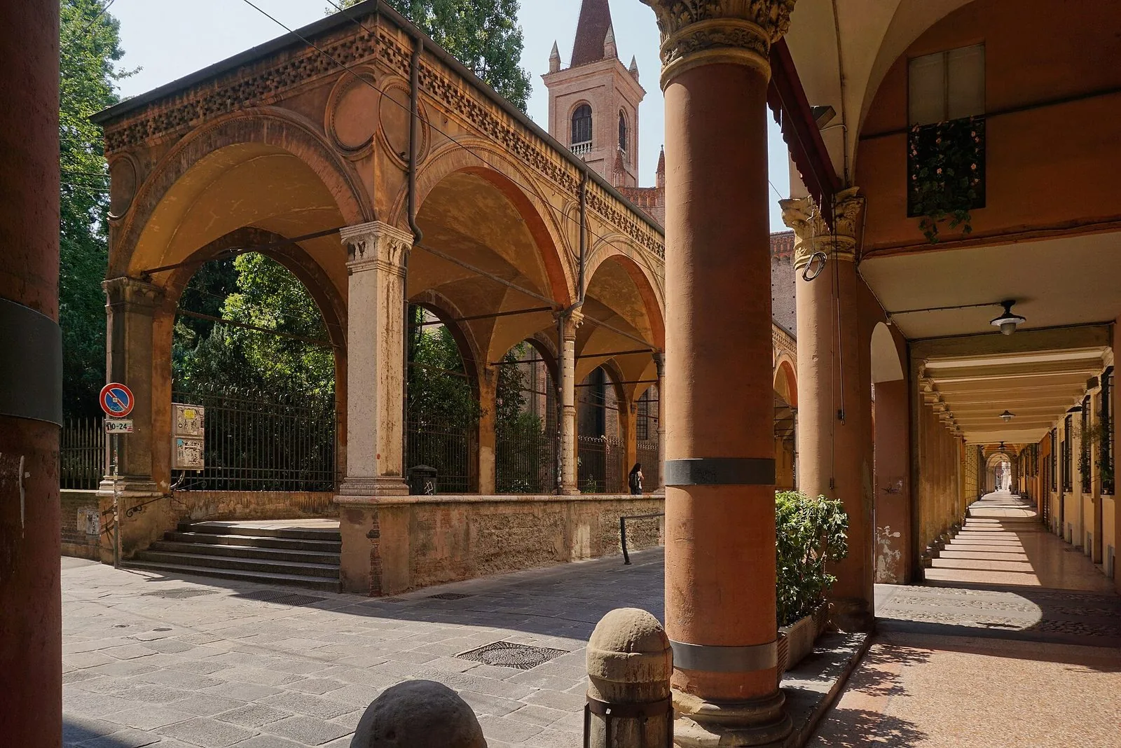 Il portico rinascimentale di Santa Maria dei Servi in Strada Maggiore, con archi in cotto e colonne chiare, il campanile sullo sfondo e a destra un lungo portico in prospettiva
