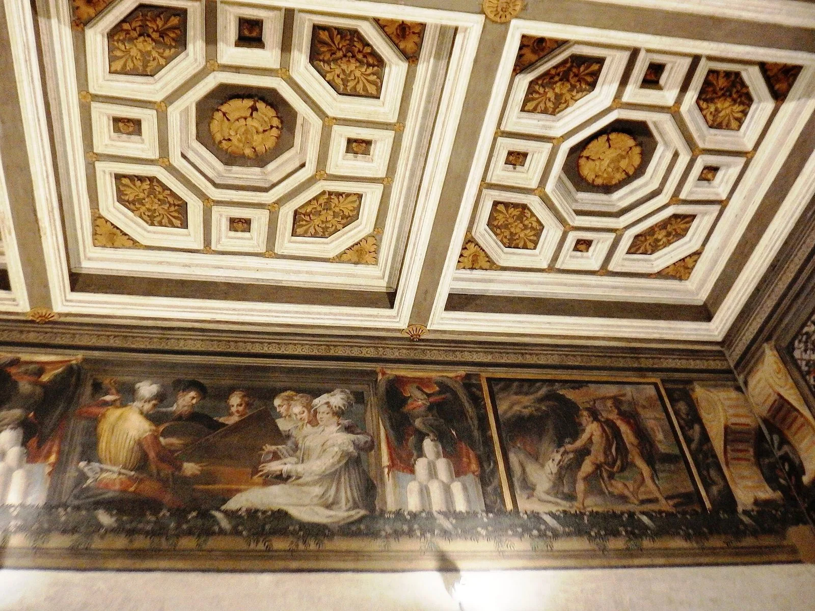 Una sala di Palazzo Poggi con il soffitto a cassettoni ottagonali bianchi e dorati e, sotto, un fregio affrescato con musici e dame attorno a una spinetta e una scena con Ercole