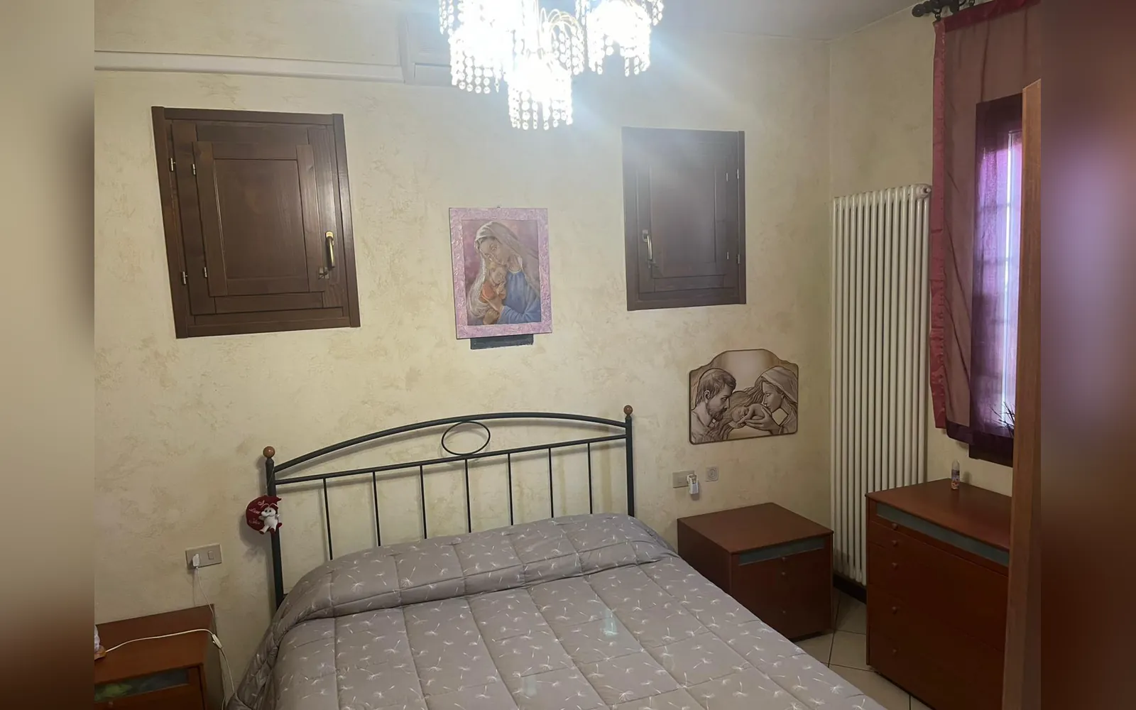 La camera matrimoniale con il letto in ferro battuto nero e il copriletto grigio