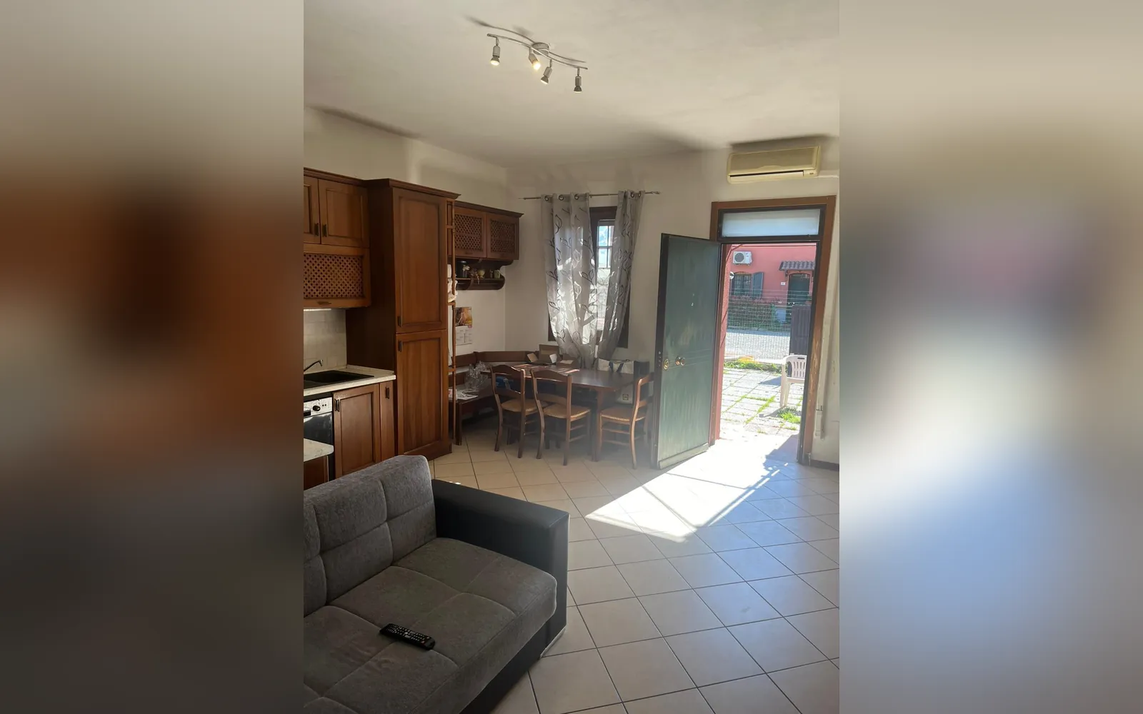 La sala con il tavolo da pranzo, l’angolo cucina e la porta d’ingresso aperta